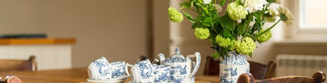 A set of white and blue china tea cups next to a vase of flowers on a wooden table