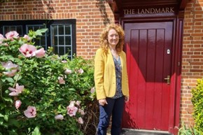 A lady wearing a yellow jacket next to a red door and surrounded by plants