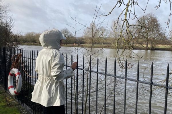 A person in a white rain jacket looking out onto the river