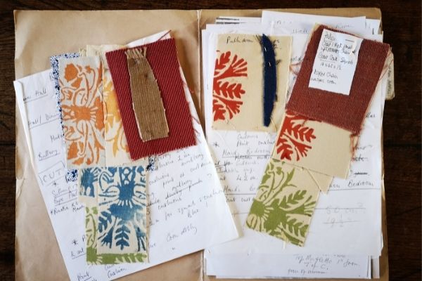 A flat lay of fabric swatches in red and gold, with leaf patterns in orange, green, red and blue.