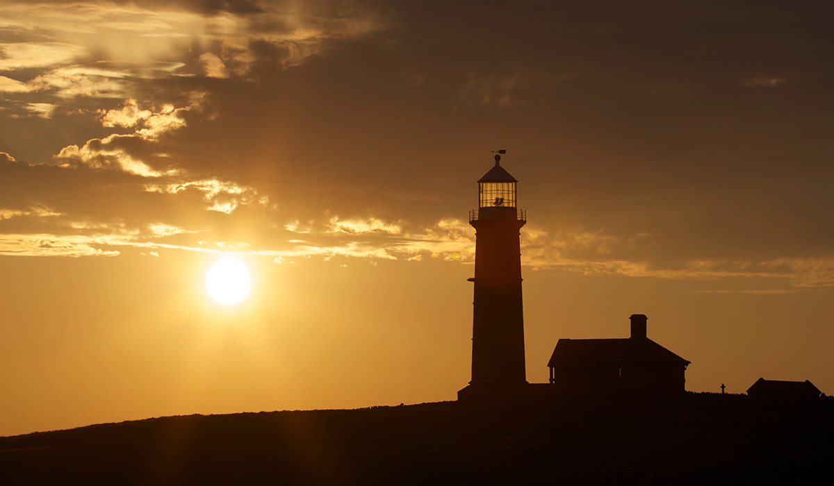 A red sunset over a sea with a dark lighthouse in shadowy foreground.