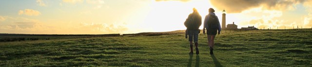 Two people walking up a hill in a sunset