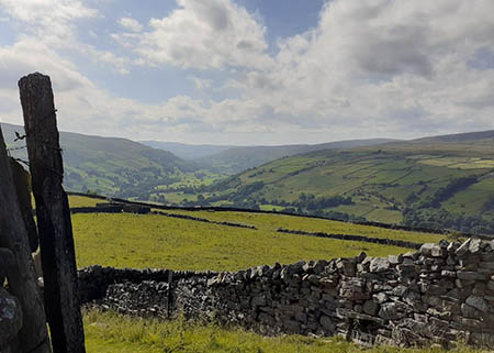 View of the Dales with a drystone wall in the foreground and patchwork hills in the distance