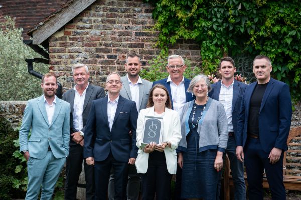 A group of smartly dressed people standing in a garden holding the award