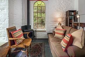 Danescombe sitting room with sofa and carved wooden chair, whitewashed walls and arched window