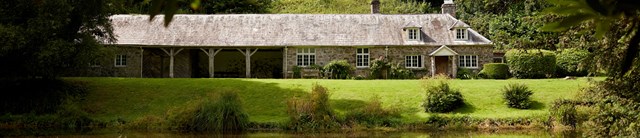 A low stone cottage in front of a pond