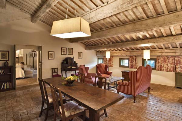 Living room with sitting area in the background, polished wooden dining table and chairs in the foreground and wooden beamed ceiling