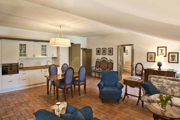 Living room with kitchen area in the background, wooden polished dining table and settee and armchair in the foreground