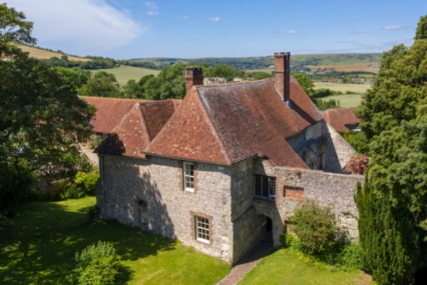 Drone photograph of large flint built house with red time rooves surrounded by trees in the sunshine