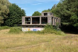 A grey, derelict building surrounded by greenery
