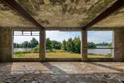 A derelict building with a view out towards trees and water